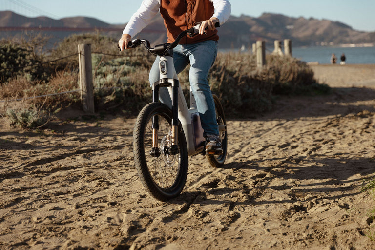 Someone riding the TM-B on a dirt path with water and hills behind them.